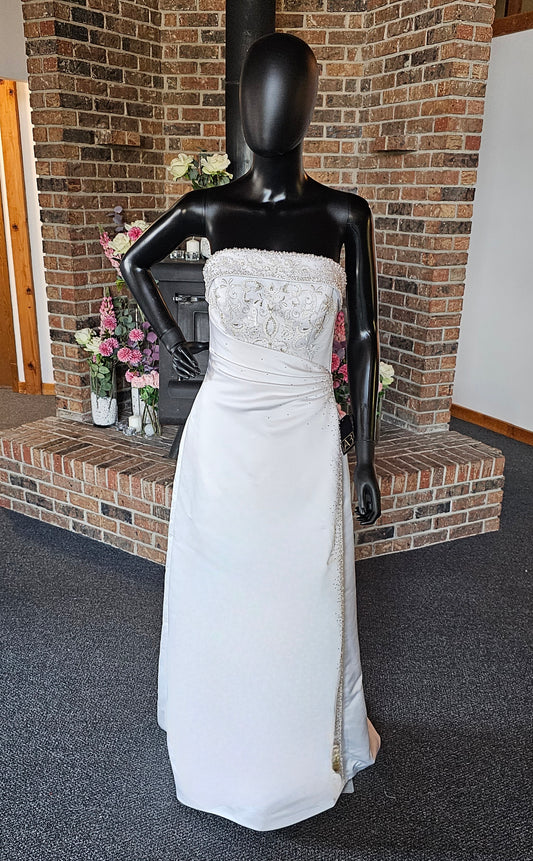 Maggie Sottero Wedding Gown  This gorgeous designer gown features a straight, banded neckline with lots of beads and embroidery. The asymmetrical side sweep adds interest and creates a lovely waistline. The creamy white satin is lustrous and falls to a small sweep train.   This gown is part of our consignment collection and has been worn before and slightly altered. It is in excellent condition and is ready to be loved again! 